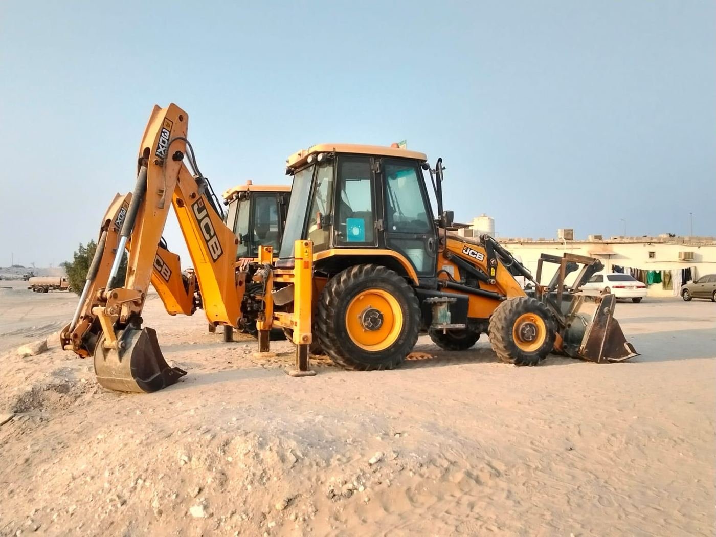 Two JCB 3CX backhoe loaders parked with stabilisers deployed in the Axom Transport yard