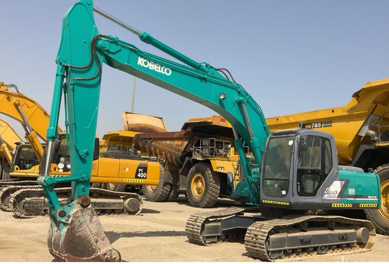 Axom Transport field technician servicing the bucket linkage and hydraulic connections on a Kobelco excavator on site